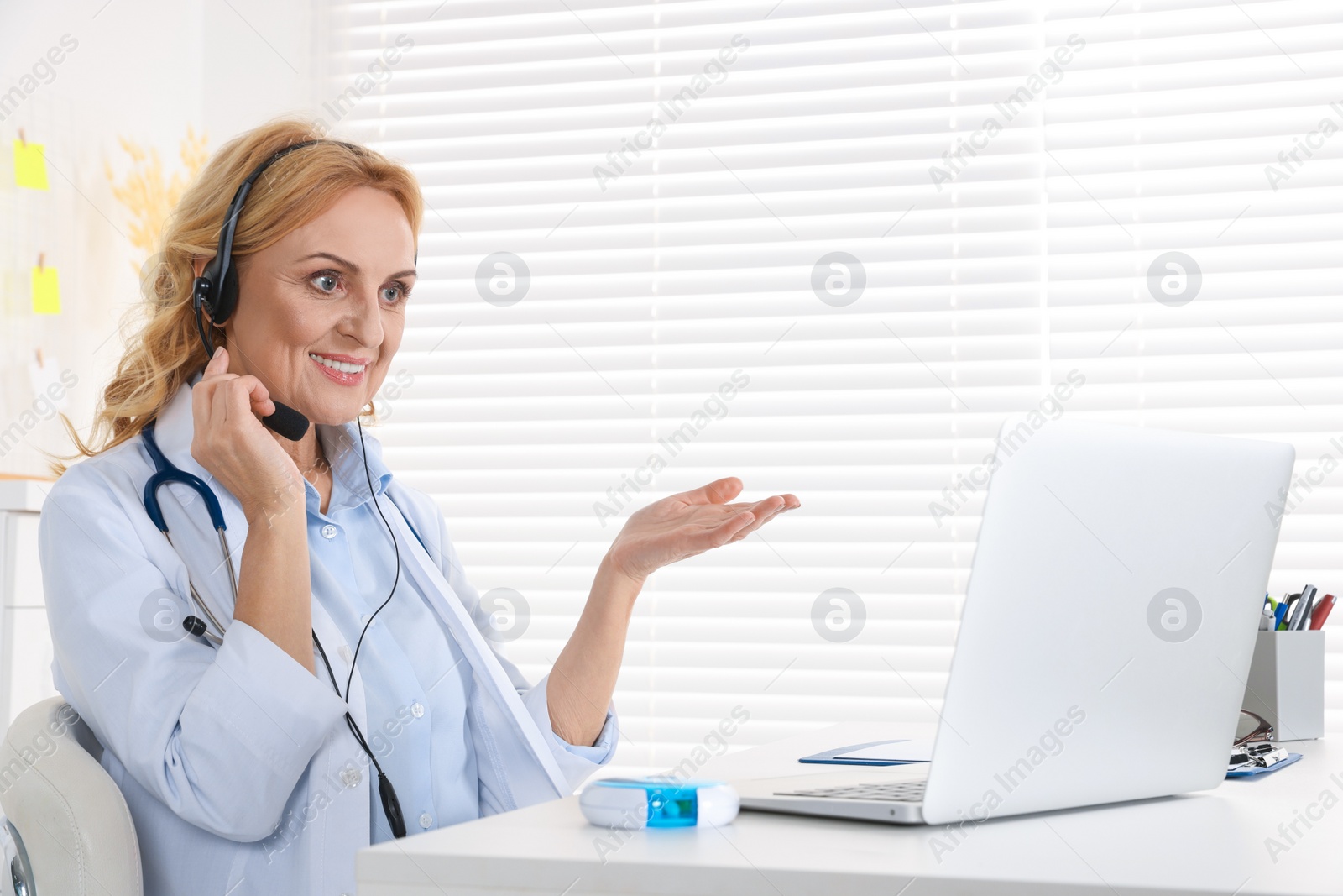 Photo of Doctor with laptop and headphones consulting patient in clinic. Online medicine concept