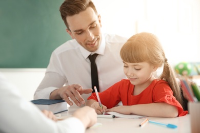 Photo of Male teacher helping girl with her task in classroom at school