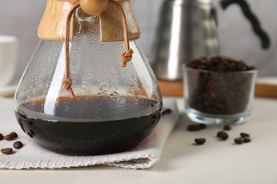 Glass chemex coffeemaker with tasty drip coffee and beans on white table, closeup