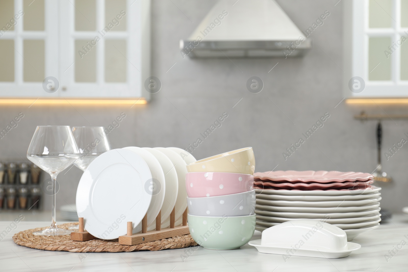 Photo of Clean plates, bowls, butter dish and glasses on white marble table in kitchen