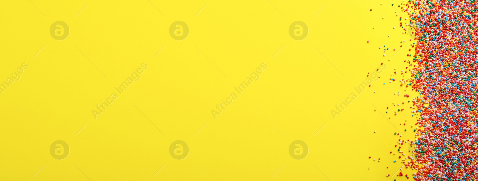 Photo of Bright colorful sprinkles on yellow background, flat lay with space for text. Confectionery decor