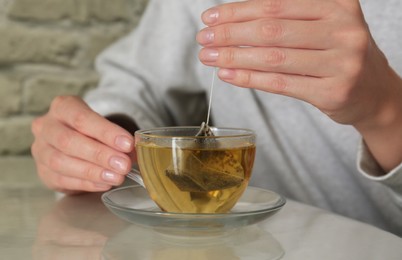 Woman taking tea bag out of cup at table indoors, closeup