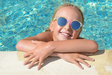 Photo of Happy cute little girl with sunglasses at edge of swimming pool on sunny day