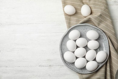 Photo of Plate with raw chicken eggs on wooden background, top view. Space for text