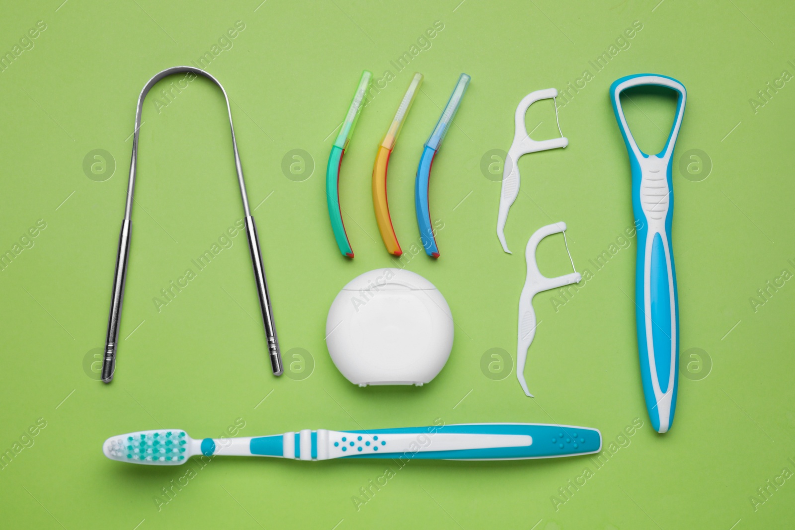 Photo of Tongue cleaners and other oral care products on light green background, flat lay