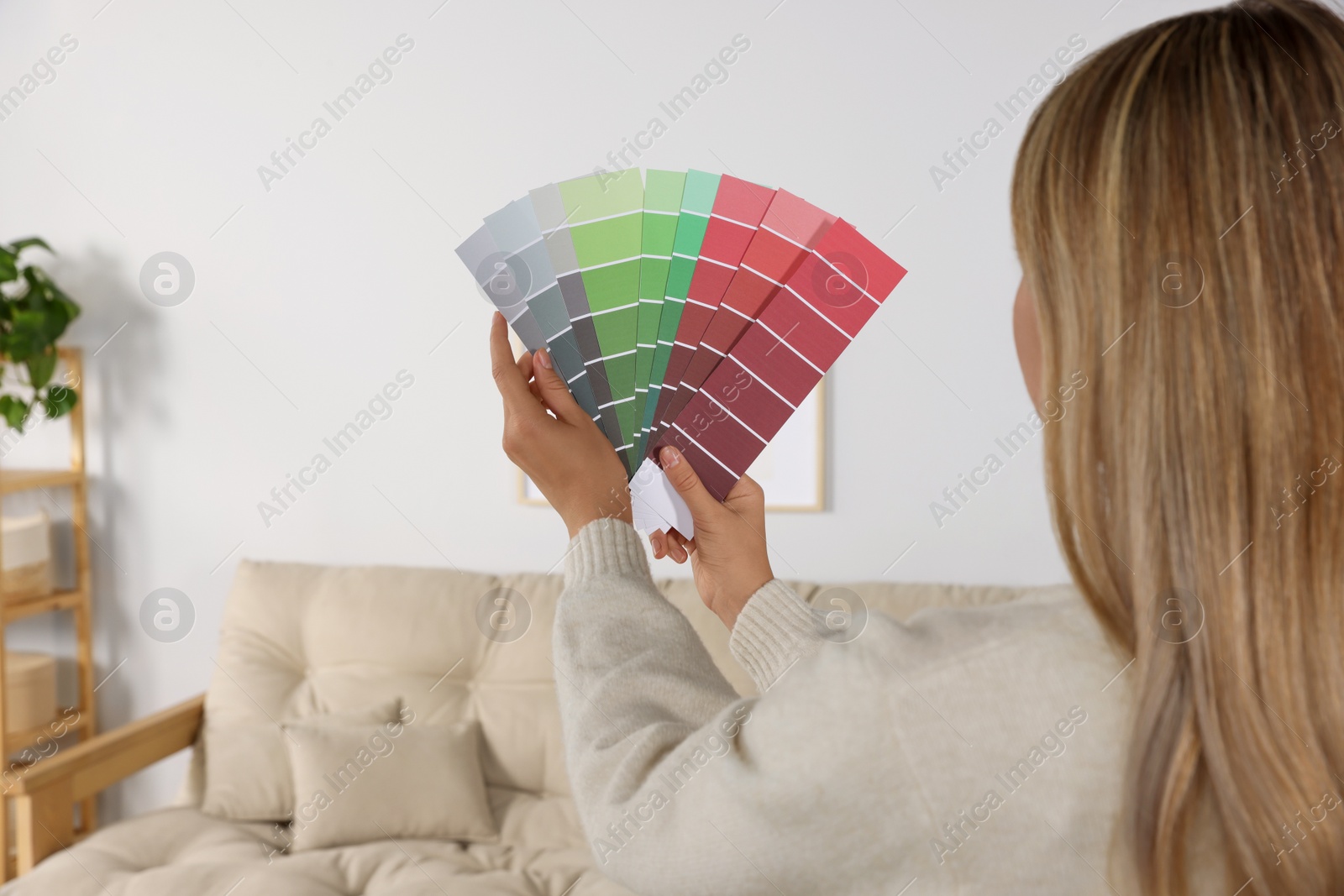 Photo of Woman choosing color for wall in room, focus on hands with paint chips. Interior design