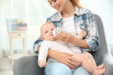 Photo of Lovely mother giving her baby drink from bottle in room