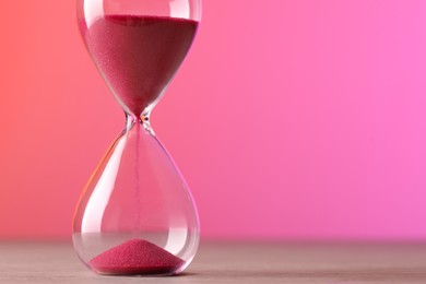 Photo of Hourglass with flowing pink sand on table against color background. Space for text