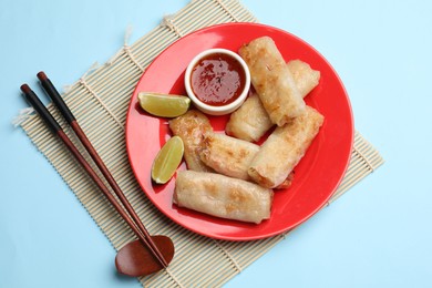 Photo of Tasty fried spring rolls, lime and sauce served on light blue table, top view