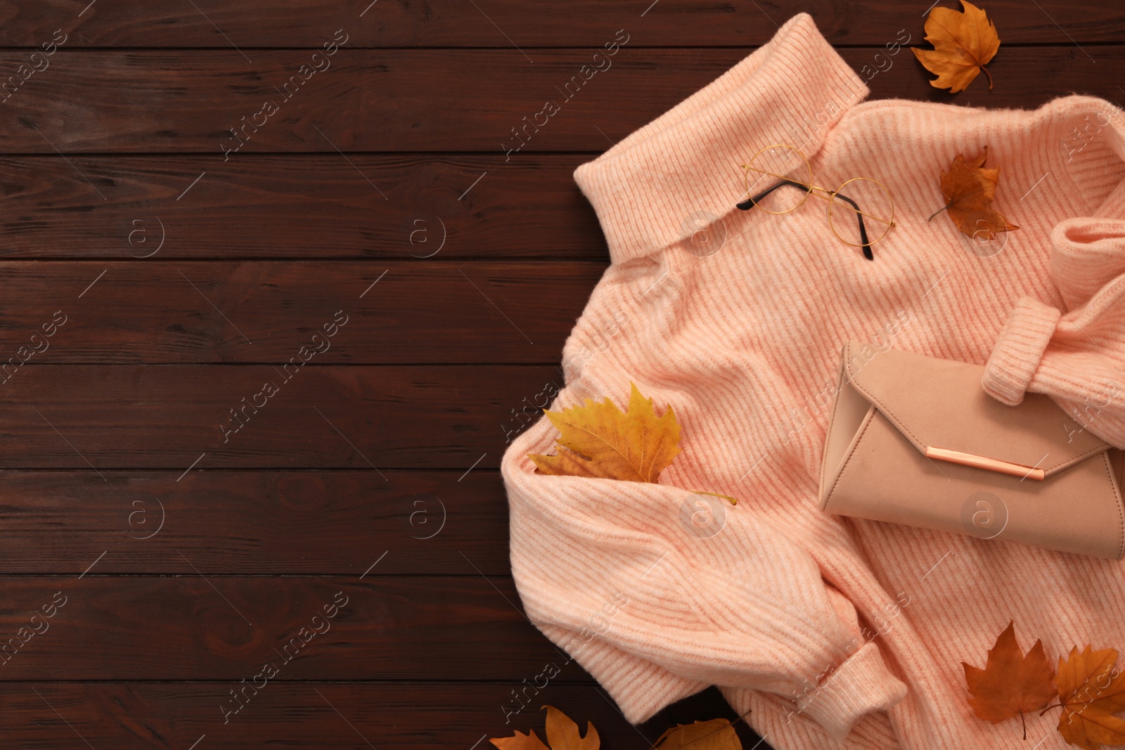 Photo of Warm sweater, bag and dry leaves on brown wooden background, flat lay with space for text. Autumn season