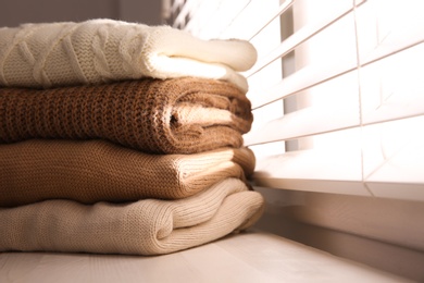 Stack of folded warm sweaters on window sill indoors, closeup. Space for text