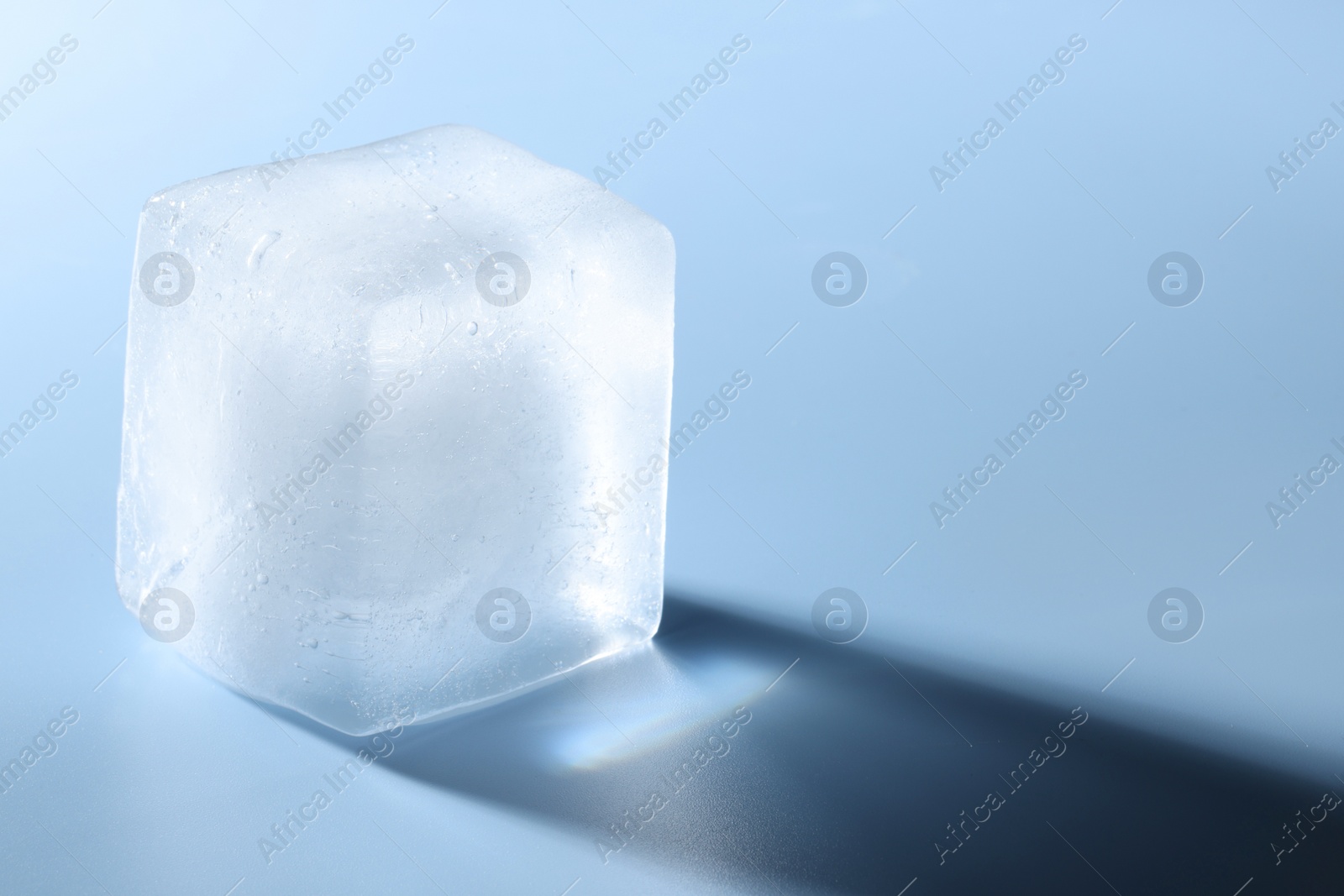 Photo of Crystal clear ice cube on light blue background, closeup. Space for text