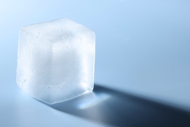 Crystal clear ice cube on light blue background, closeup. Space for text