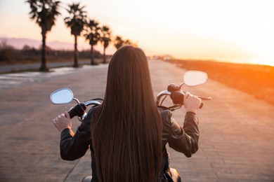 Photo of Woman riding motorcycle at sunset, back view