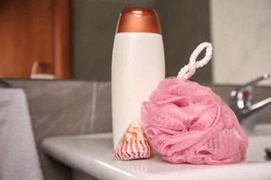 Photo of Pink sponge, seashell and shower gel bottle on washbasin in bathroom, closeup. Space for text