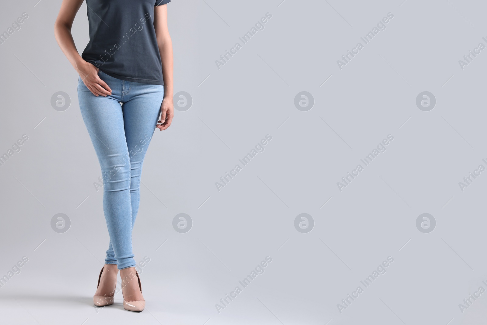 Photo of Woman wearing stylish jeans and high heels shoes on light gray background, closeup. Space for text