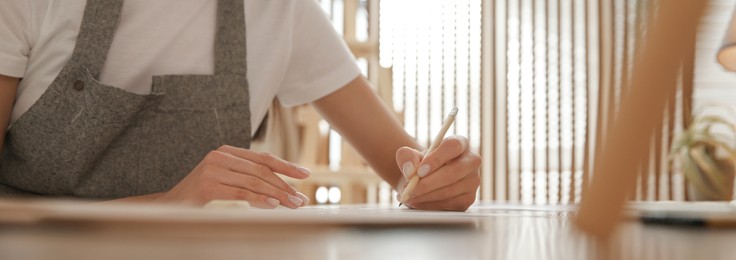 Image of Young woman drawing with pencil at table indoors, closeup. Banner design