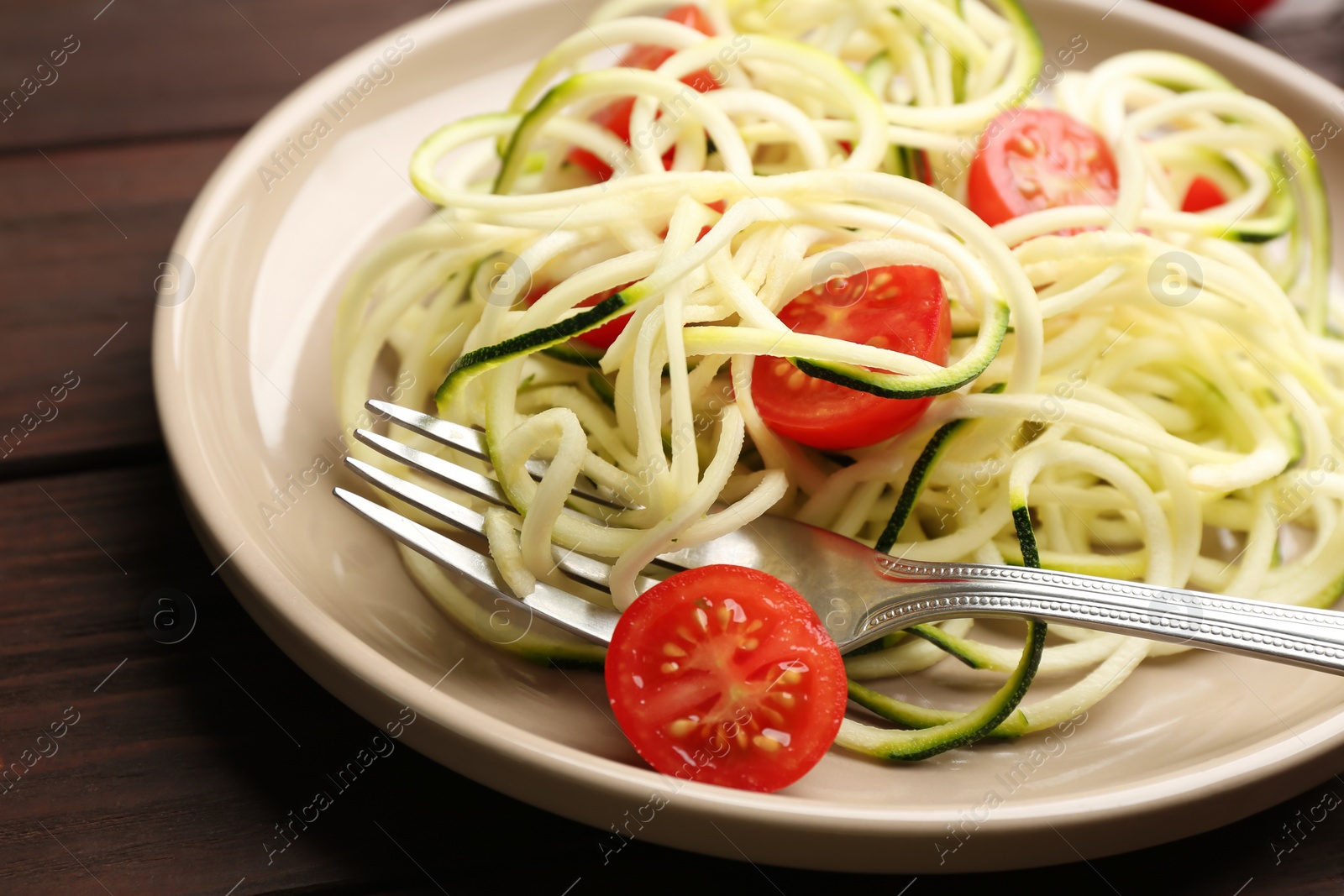 Photo of Delicious zucchini pasta with cherry tomatoes on wooden table, closeup