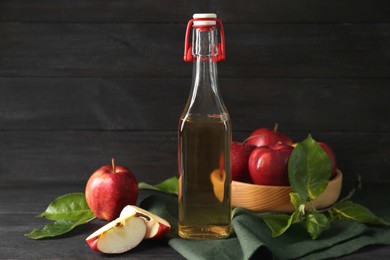 Bottle of delicious cider, cut and whole apples with green leaves on black wooden table