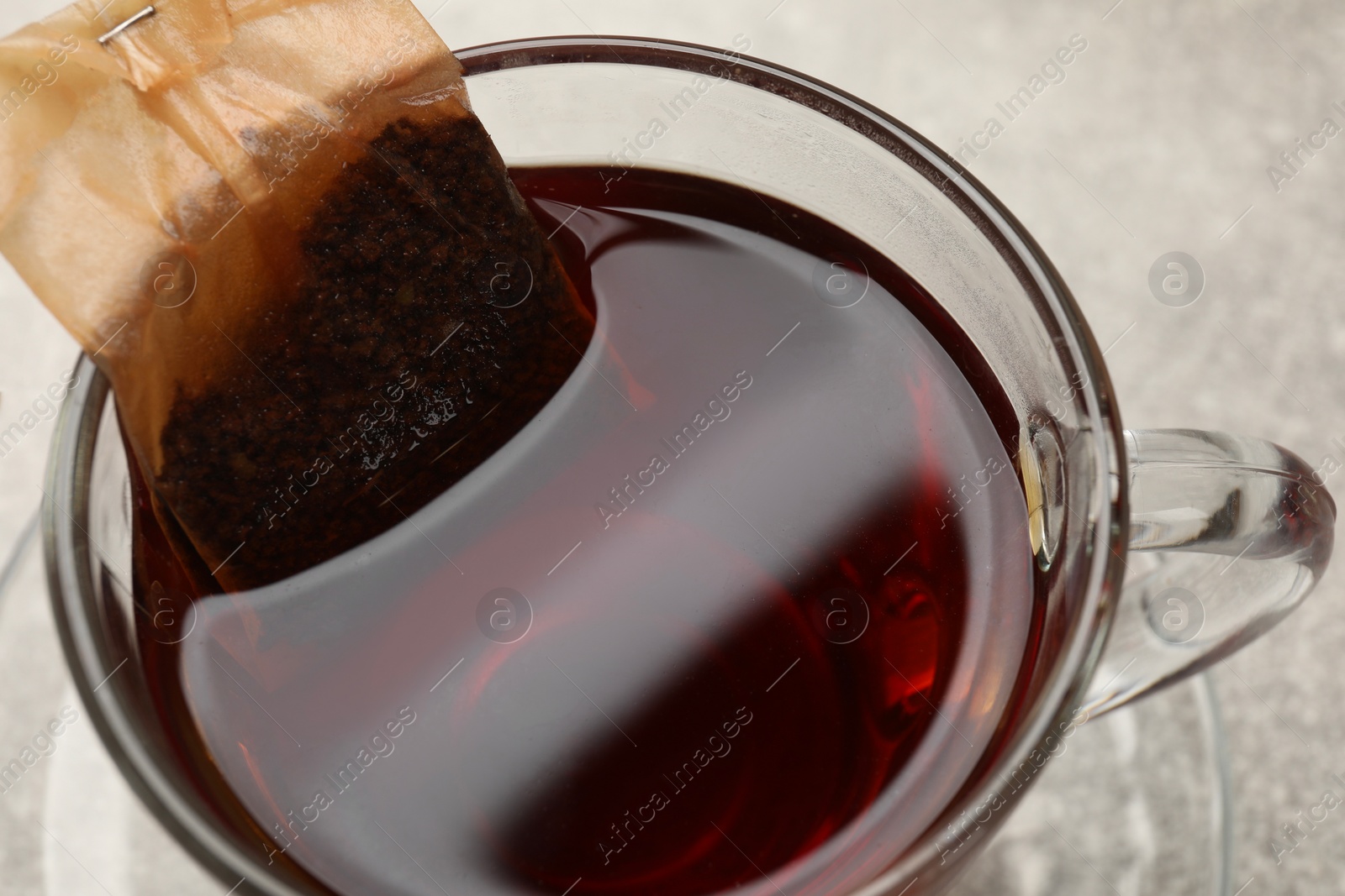 Photo of Brewing tea. Glass cup with tea bag on table, closeup