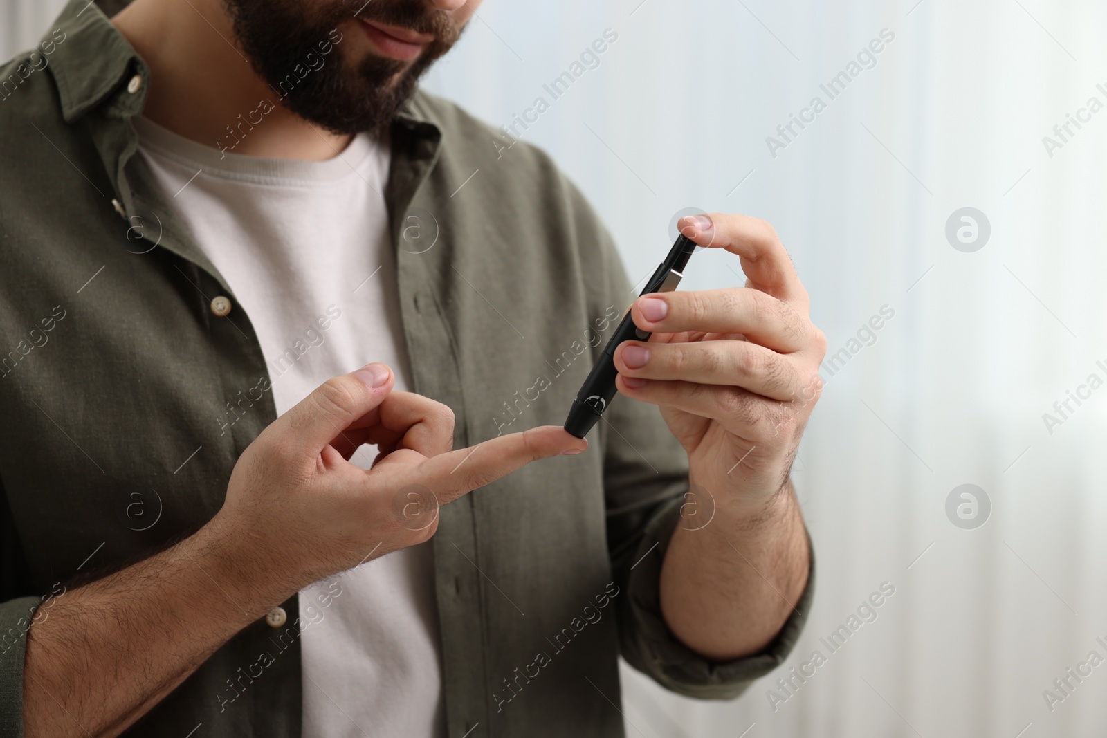 Photo of Diabetes test. Man checking blood sugar level with lancet pen at home, closeup