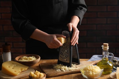 Woman grating cheese at wooden table, closeup