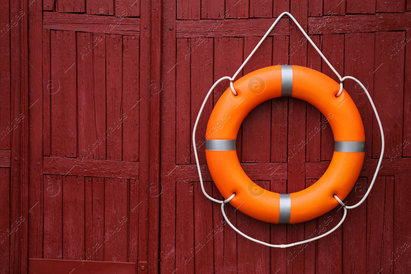 Photo of Orange life buoy hanging on red wooden wall, space for text