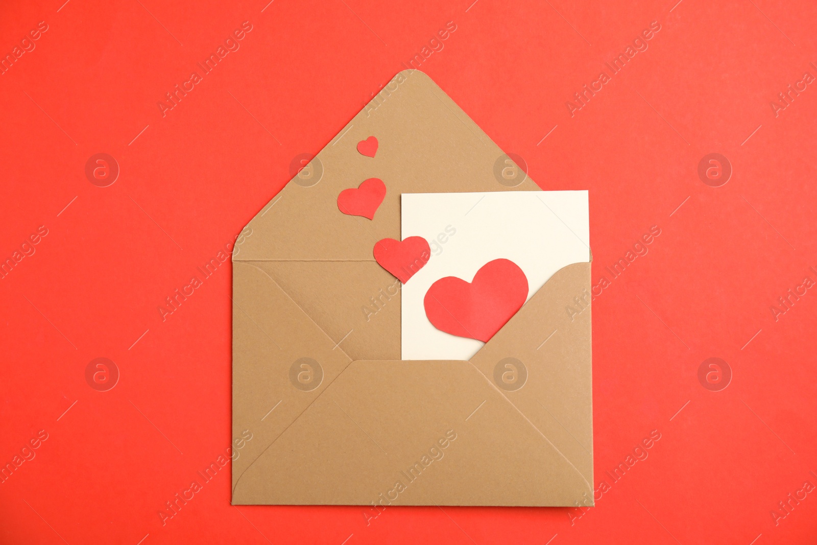 Photo of Envelope with card and paper hearts on red background, top view. Love letter