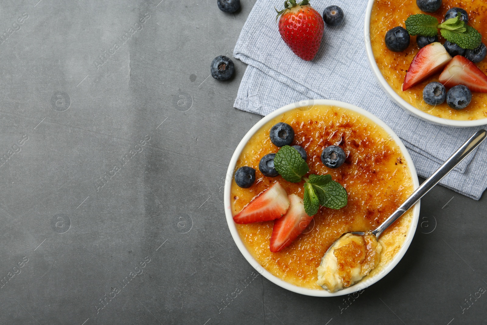 Photo of Delicious creme brulee with berries and mint in bowls on grey table, flat lay. Space for text