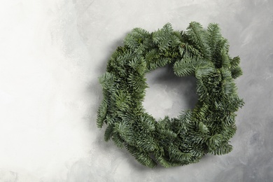 Photo of Christmas wreath made of fir tree branches on light grey background, space for text