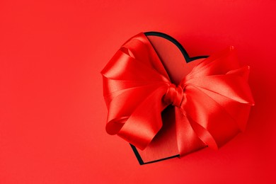 Photo of Beautiful heart shaped gift box with bow on red background, top view