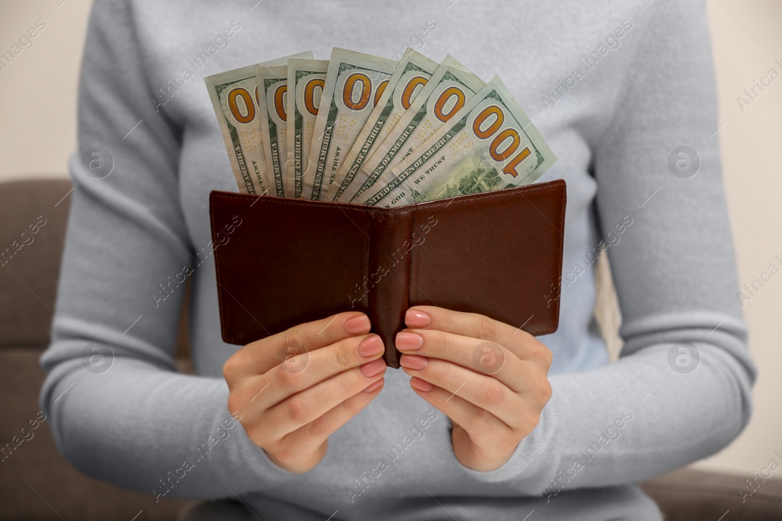 Photo of Woman holding brown leather wallet with dollars indoors, closeup. Money exchange