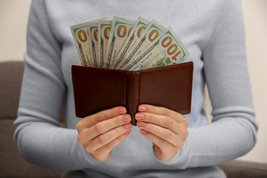 Woman holding brown leather wallet with dollars indoors, closeup. Money exchange