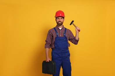 Professional builder in uniform with hammer and toolbox on yellow background
