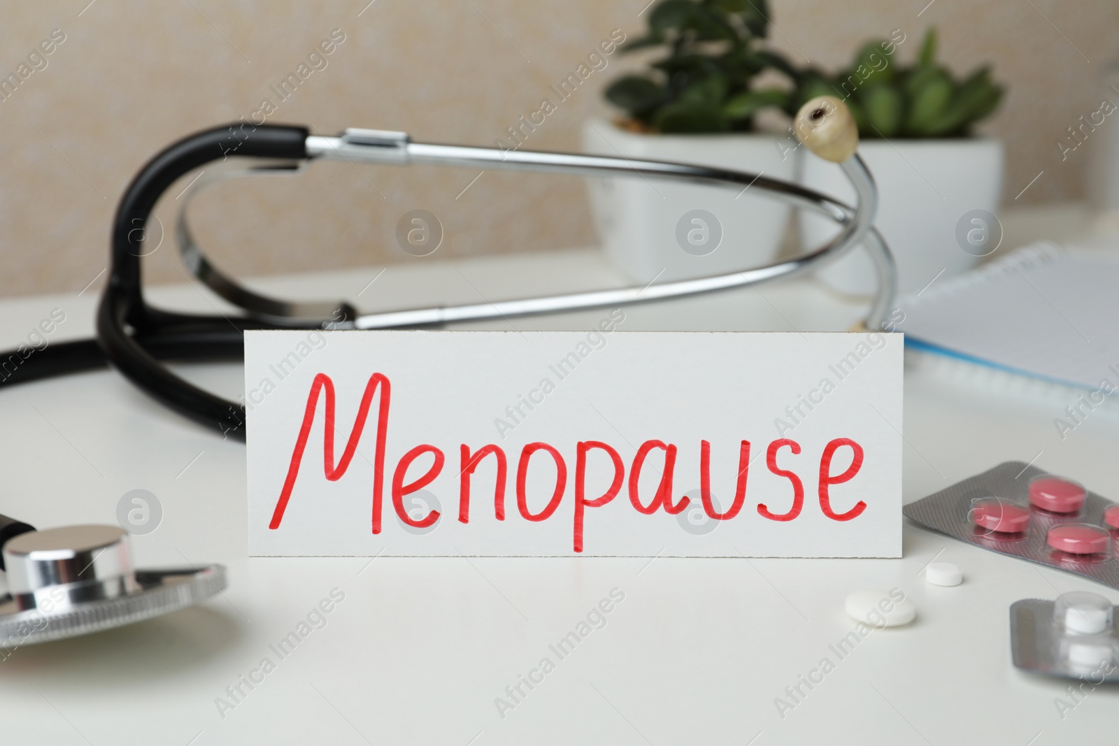 Photo of Card with word Menopause, pills and stethoscope on white table