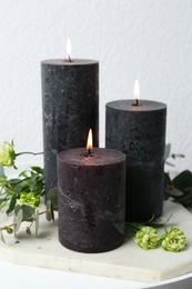 Burning candles, flowers and green branches on table at white wall