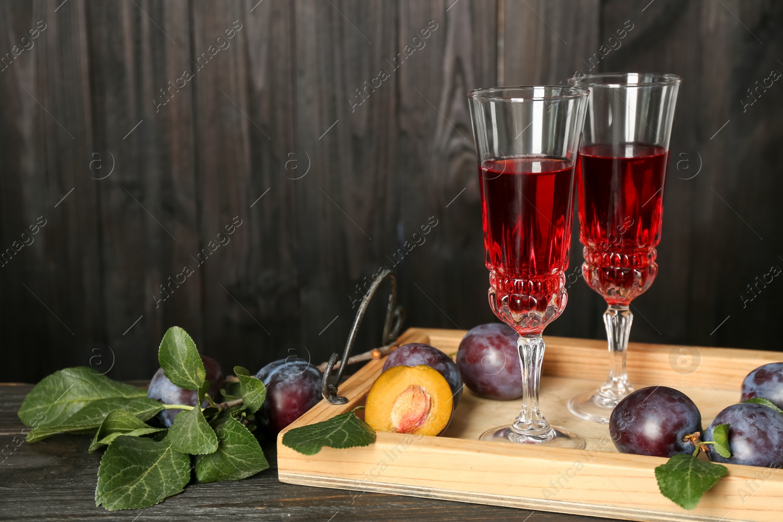 Photo of Delicious plum liquor and ripe fruits on black wooden table. Homemade strong alcoholic beverage