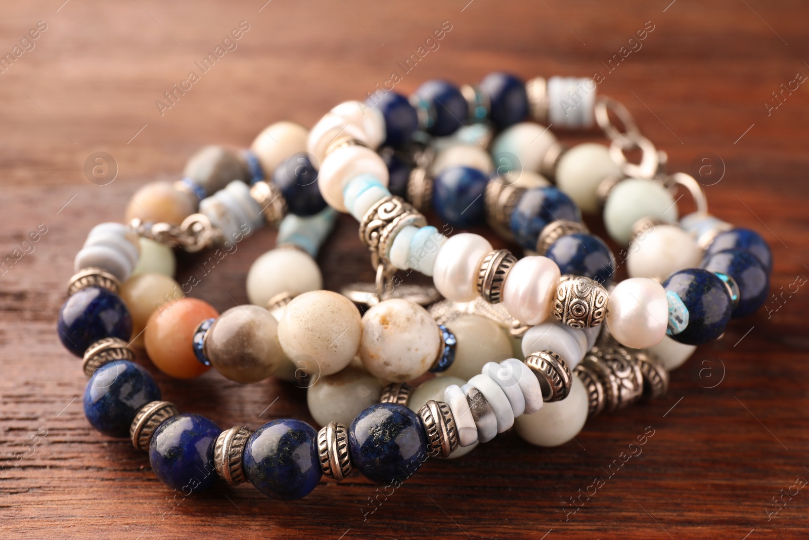 Photo of Beautiful bracelets with gemstones on wooden table, closeup