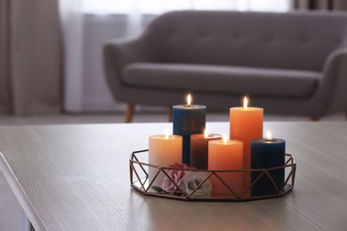 Tray with burning candles and flowers on table in living room