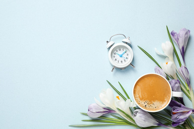 Cup of morning coffee, crocuses and alarm clock on light background, flat lay. Space for text