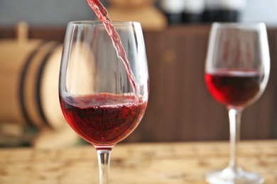 Photo of Pouring delicious red wine into glass on table, closeup