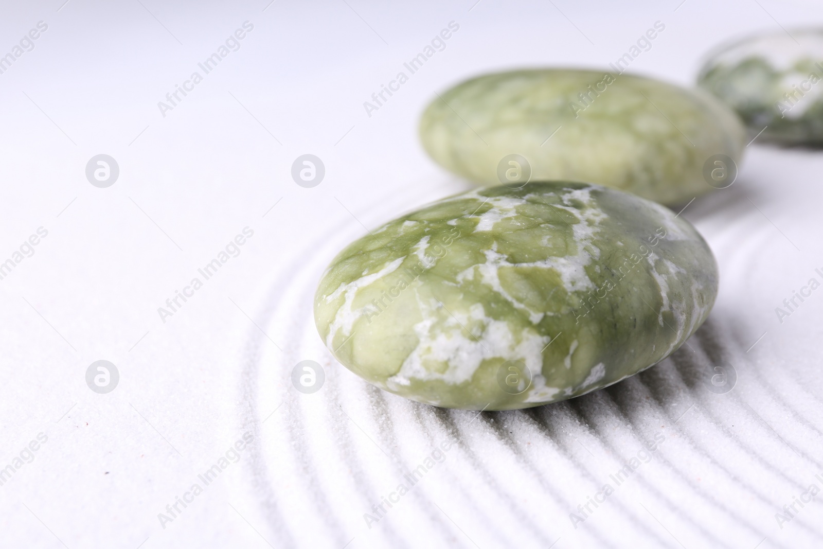 Photo of Zen garden stones on white sand with pattern, closeup. Space for text