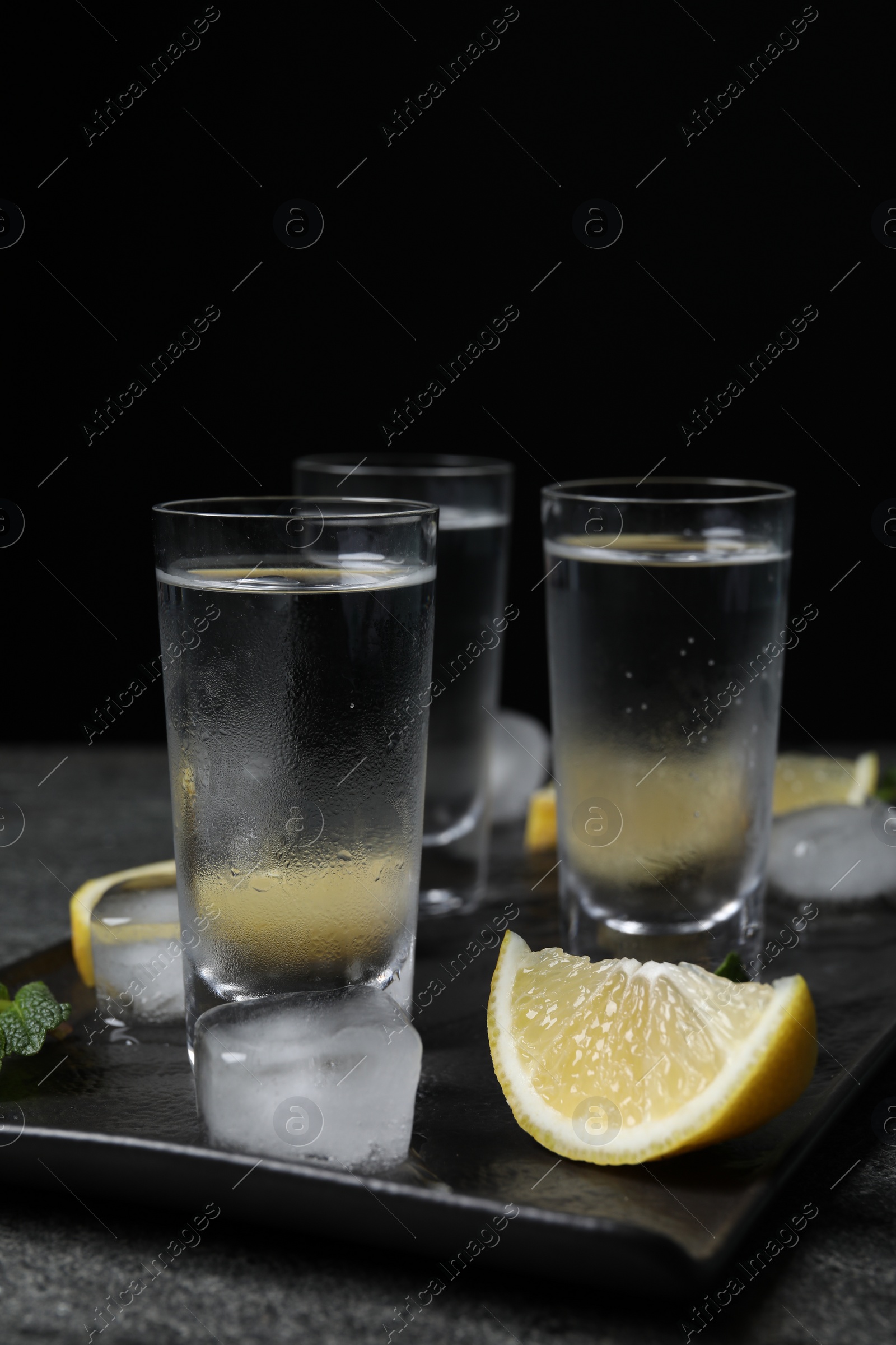 Photo of Shot glasses of vodka with lemon slices, mint and ice on grey table