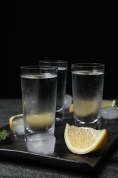 Photo of Shot glasses of vodka with lemon slices, mint and ice on grey table