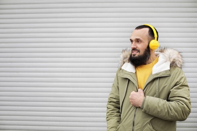 Photo of Mature man with headphones listening to music near light wall. Space for text