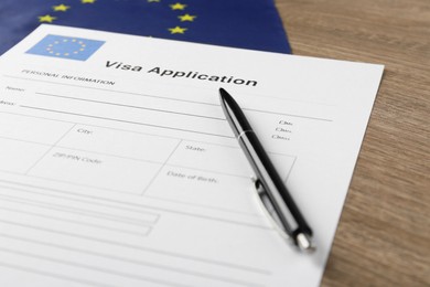 Immigration to Europe. Visa application form, flag and pen on wooden table, closeup