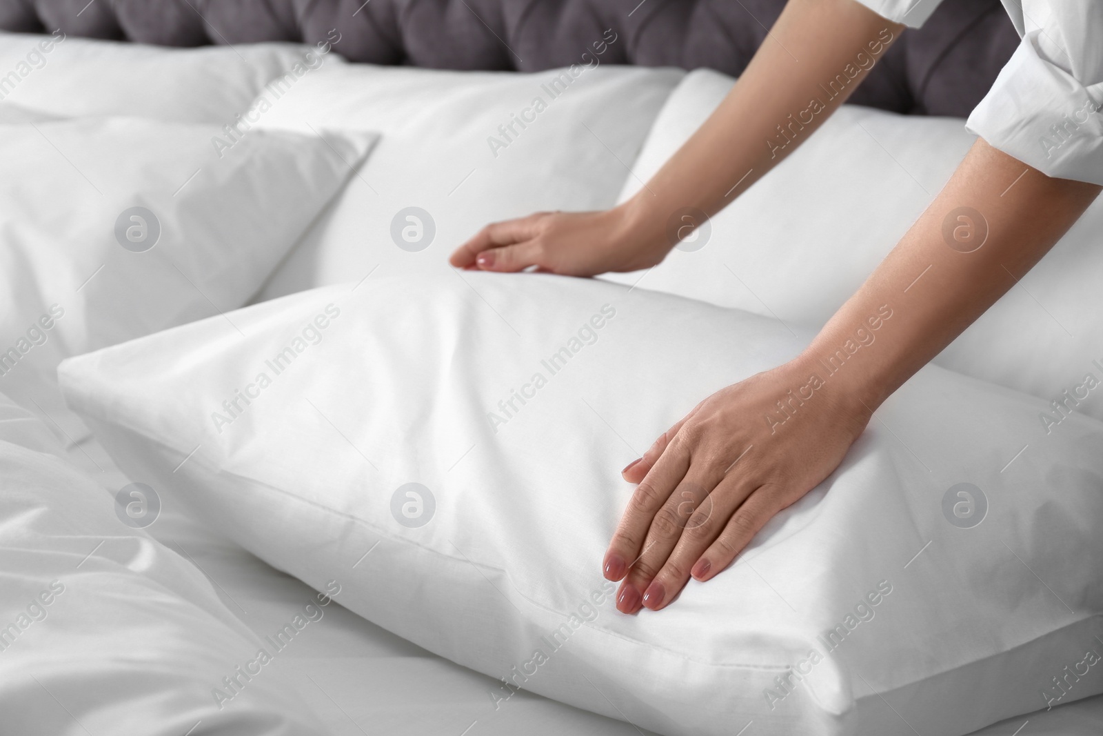 Photo of Woman fluffing soft pillow in bedroom, closeup