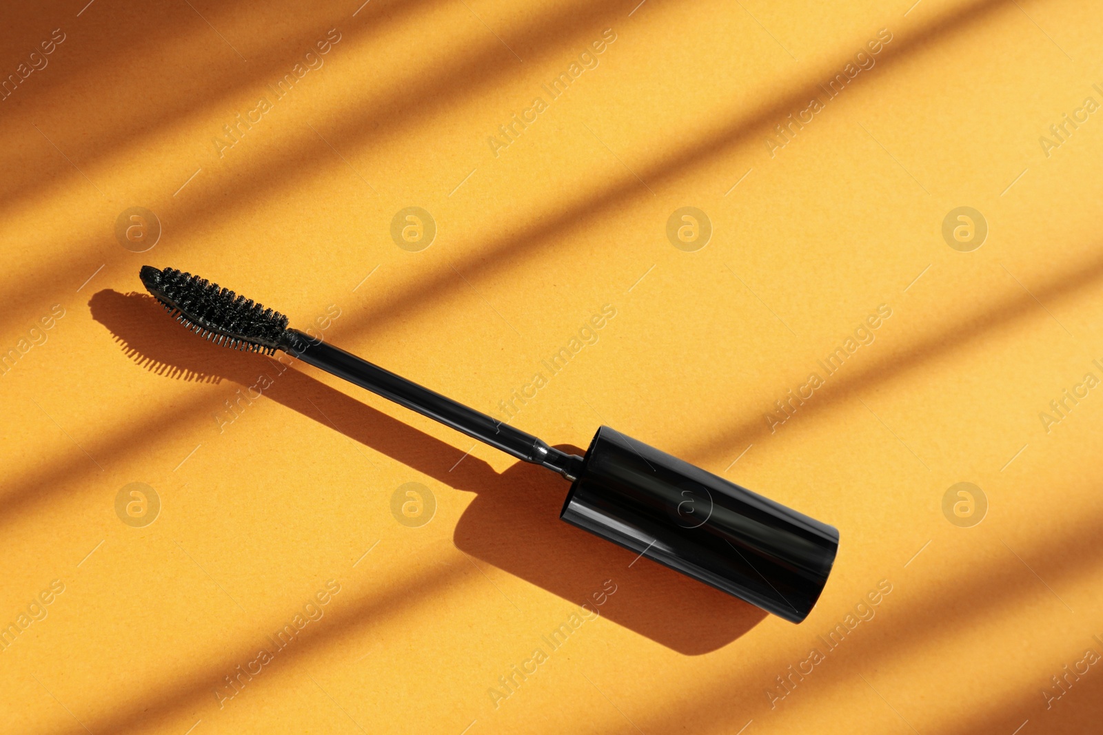 Photo of Mascara wand on orange background, top view. Makeup product
