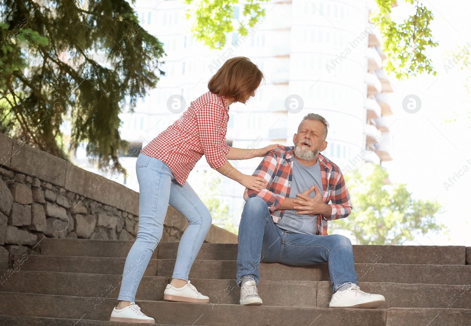 Photo of Woman helping mature man suffering from heart attack on stairs, outdoors