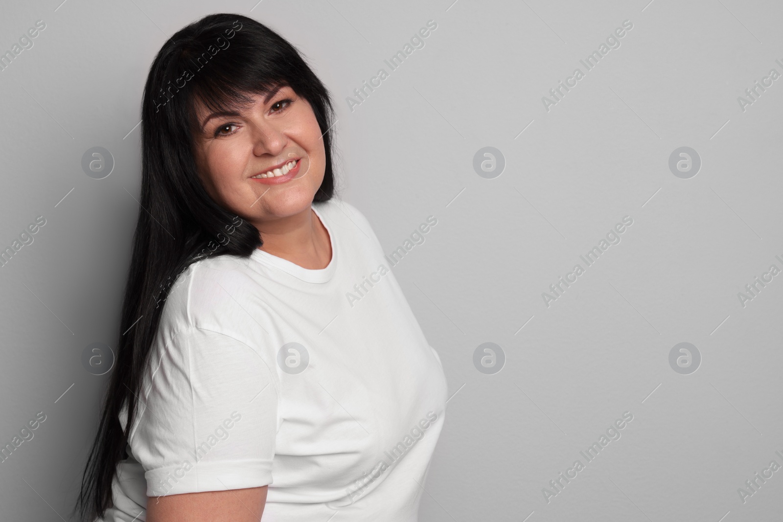 Photo of Beautiful overweight mature woman with charming smile on light grey background. Space for text